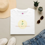 Small But Fierce Women's Minimalist T-Shirt laid flat with accessories and a flower design.
